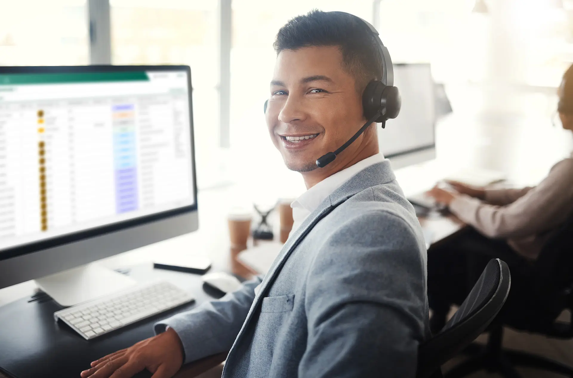 Smiling call center agent with headset at computer.