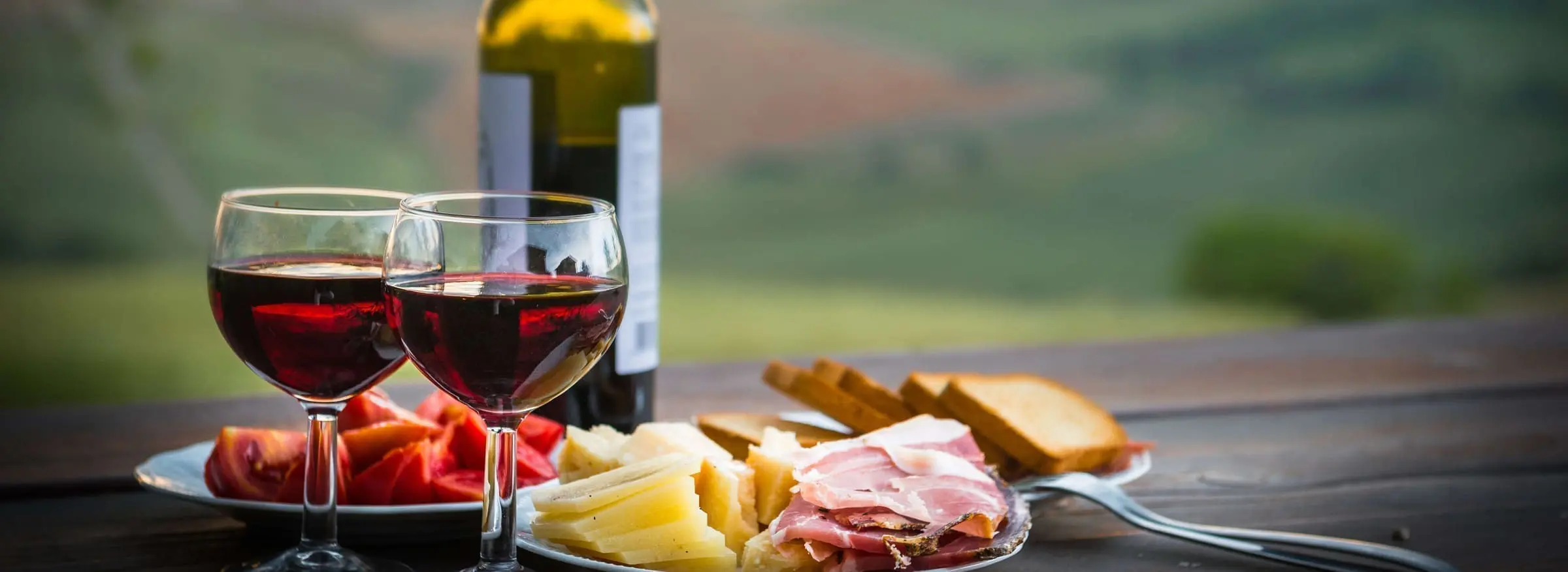 Red wine with cheese and prosciutto on table.