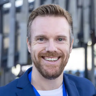 Smiling man wearing blue jacket outdoors.