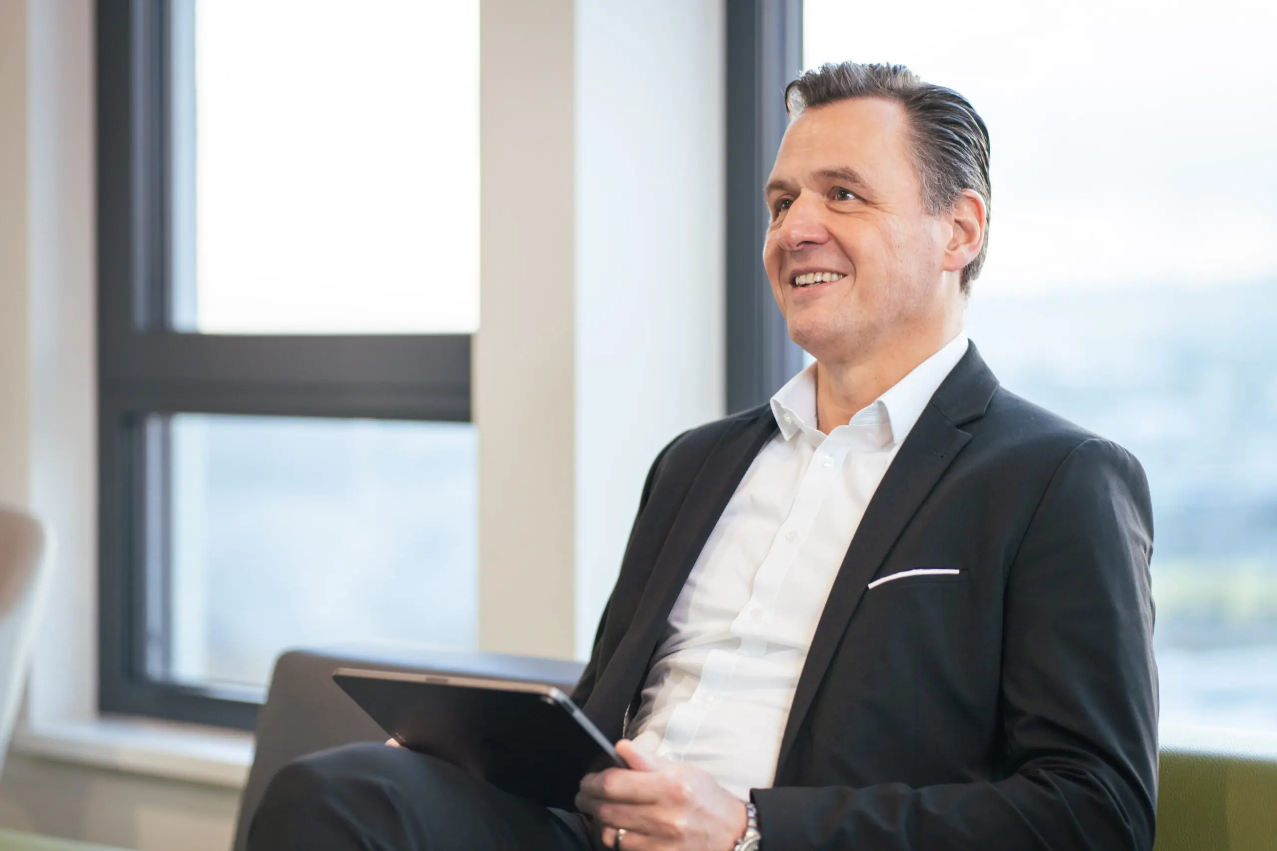 Businessman smiling with tablet near window.