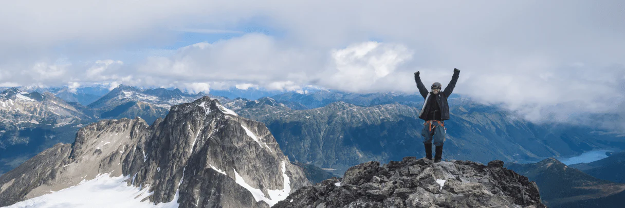 Person celebrating atop snowy mountain peak.