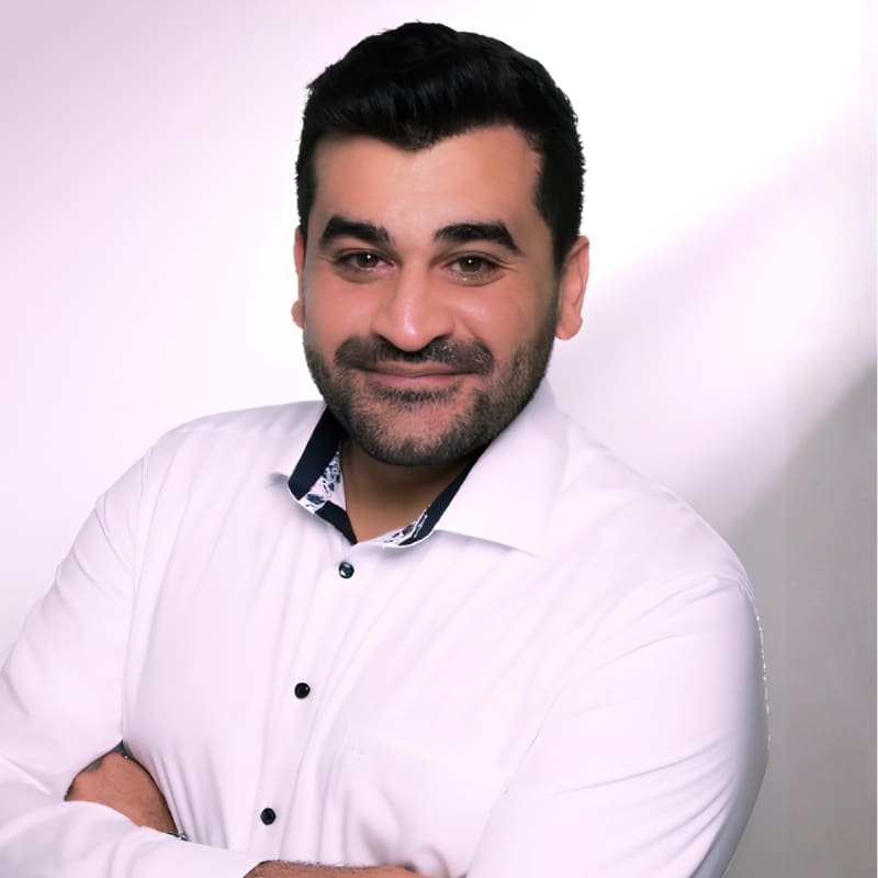 Smiling man in white shirt with crossed arms.