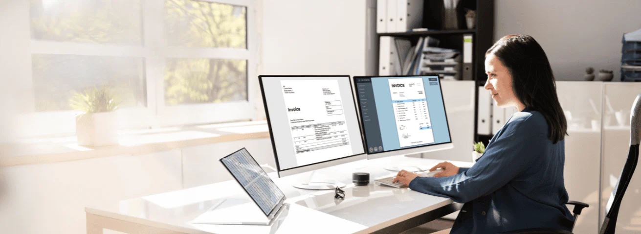 Woman reviewing documents on dual computer monitors.
