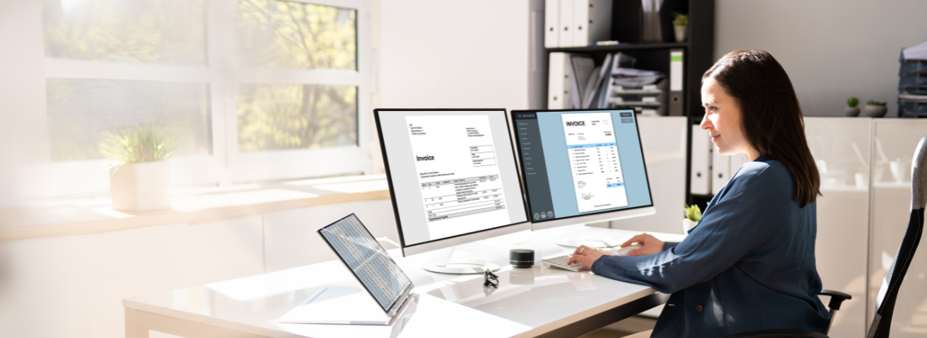 Woman reviewing documents on dual computer monitors.