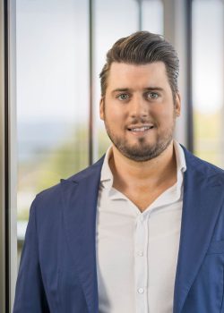 Man in blue suit smiling indoors.