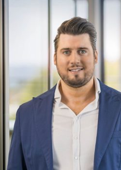 Man in blue suit smiling indoors.