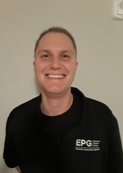 Smiling man in EPG shirt next to wall speaker.
